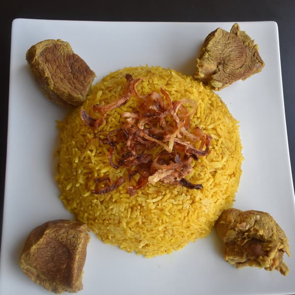 Middle Eastern dish with yellow rice topped with fried onions, surrounded by four pieces of meat.
