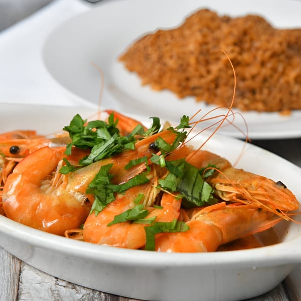 A white bowl of King of Koshary's shrimp with parsley, and a blurred dish of rice in the background.