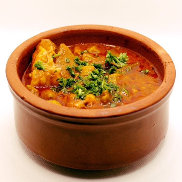 A clay bowl filled with a rich, red Middle Eastern stew, garnished with fresh parsley.